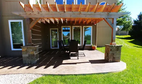Wooden pergola structure with climbing plants over a stone patio area featuring outdoor seating and dining set surrounded by landscaped garden beds